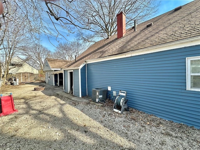 view of property exterior featuring central AC, roof with shingles, and a chimney