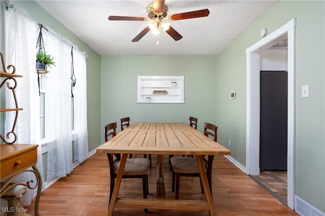 dining room featuring baseboards, a textured ceiling, a ceiling fan, and light wood finished floors