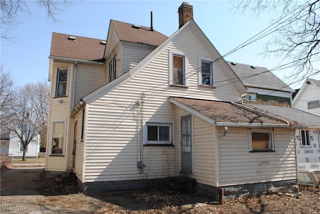 back of property with entry steps, roof with shingles, and a chimney