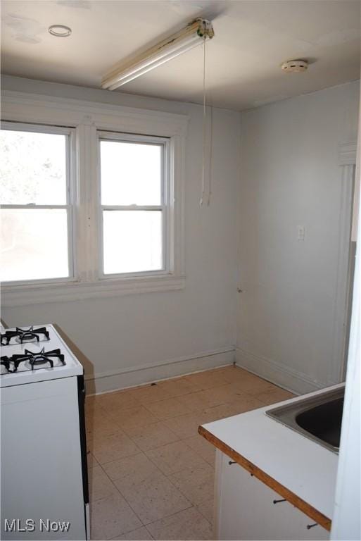 kitchen featuring a sink, baseboards, and white gas range oven