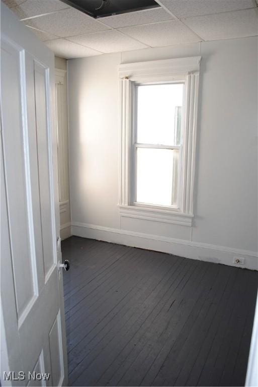 empty room featuring dark wood-style floors, a drop ceiling, and baseboards