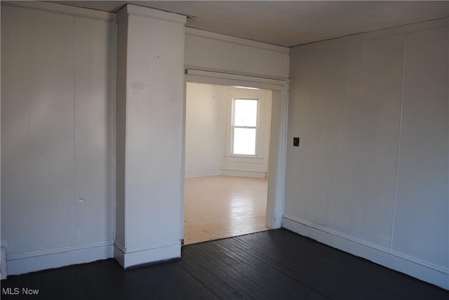 spare room featuring dark wood-style flooring and a decorative wall