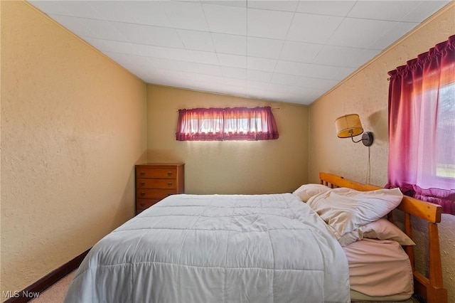 bedroom featuring lofted ceiling and a textured wall