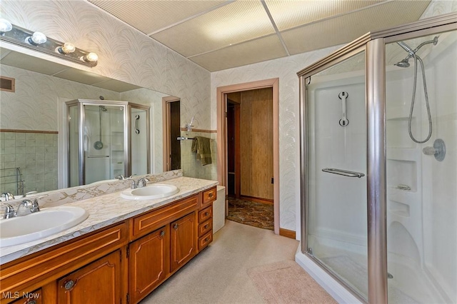 bathroom with double vanity, a shower stall, wallpapered walls, and a sink