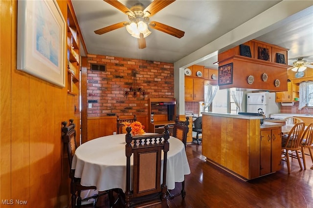 dining area with dark wood finished floors, visible vents, a ceiling fan, and wooden walls