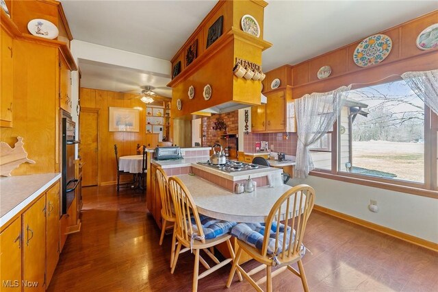 dining space featuring dark wood-type flooring, wooden walls, a toaster, baseboards, and ceiling fan