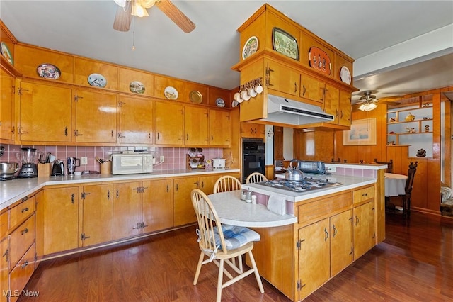 kitchen featuring stainless steel gas cooktop, dark wood-style flooring, ceiling fan, under cabinet range hood, and black oven