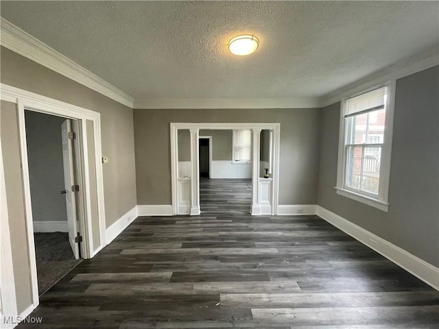 spare room with a textured ceiling, crown molding, baseboards, and dark wood-style flooring