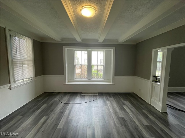 spare room with beamed ceiling, a wainscoted wall, visible vents, a textured ceiling, and dark wood-style floors