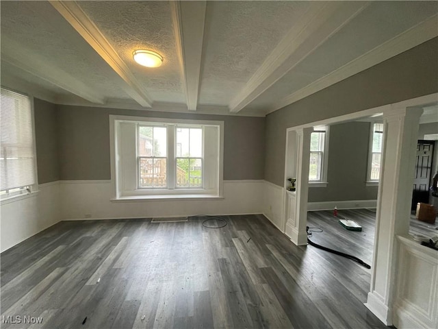 spare room with a wainscoted wall, decorative columns, dark wood-style flooring, a textured ceiling, and beamed ceiling