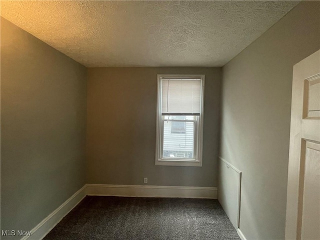 empty room with dark carpet, a textured ceiling, and baseboards