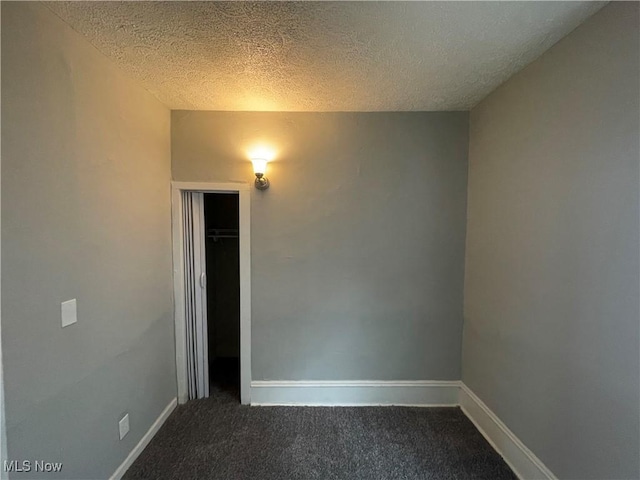 empty room with baseboards, dark colored carpet, and a textured ceiling