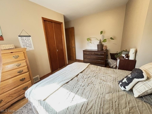 bedroom with a closet, visible vents, baseboards, and wood finished floors