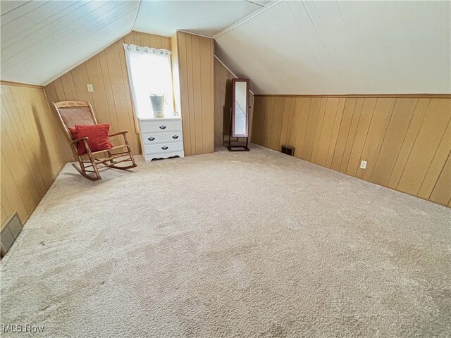 additional living space with vaulted ceiling, carpet, visible vents, and wood walls