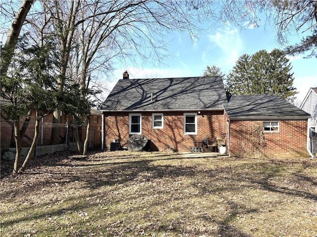 back of property with brick siding, a shingled roof, a chimney, and fence