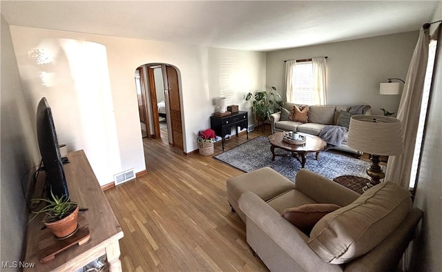 living area featuring wood finished floors, arched walkways, visible vents, and baseboards