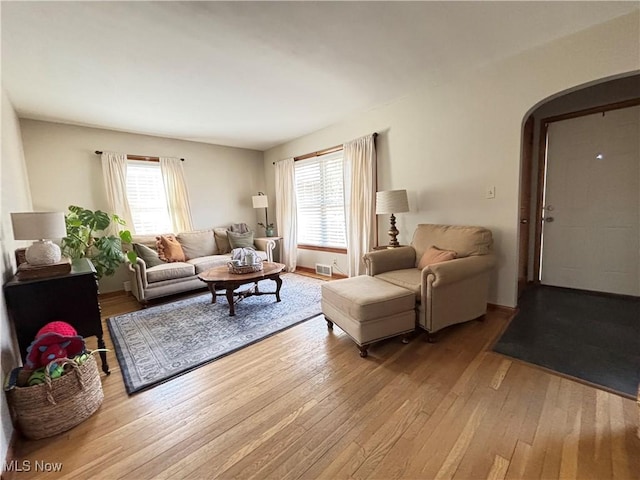 living area with visible vents, arched walkways, and light wood finished floors