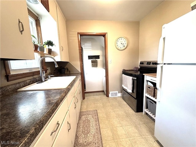 kitchen with visible vents, electric stove, a sink, dark countertops, and freestanding refrigerator