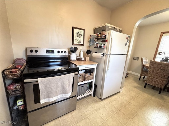 kitchen with electric range, baseboards, arched walkways, and freestanding refrigerator