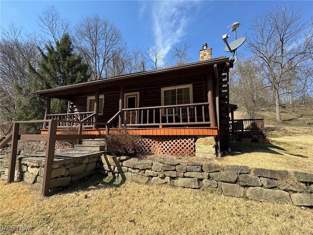 log cabin featuring a wooden deck, log siding, and a chimney