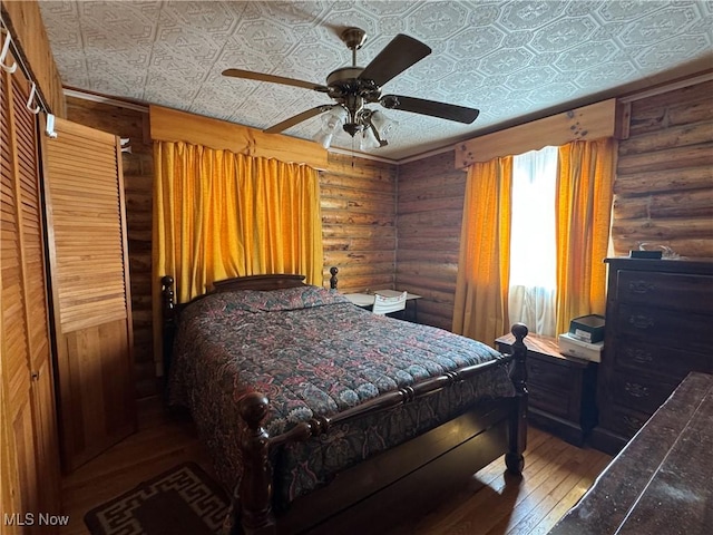 bedroom featuring an ornate ceiling, log walls, a ceiling fan, and hardwood / wood-style floors