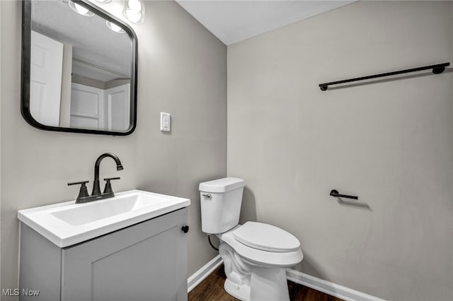 half bath with toilet, vanity, baseboards, and wood finished floors