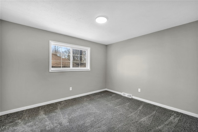 spare room featuring visible vents, baseboards, and dark carpet