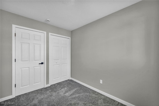 unfurnished bedroom with baseboards, dark colored carpet, and a closet