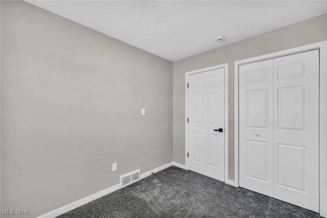 unfurnished bedroom featuring a closet, visible vents, baseboards, and dark carpet