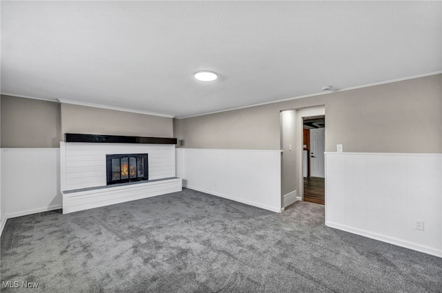 unfurnished living room with carpet flooring, wainscoting, crown molding, and a glass covered fireplace