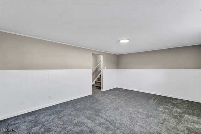 spare room featuring wainscoting, dark carpet, and stairs