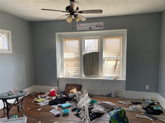 interior space with a textured ceiling, a ceiling fan, baseboards, and wood finished floors