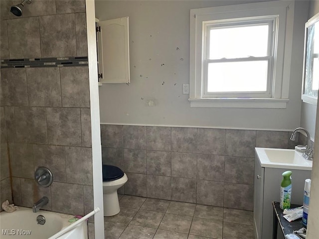 bathroom with a wainscoted wall, toilet, bathing tub / shower combination, tile patterned floors, and tile walls