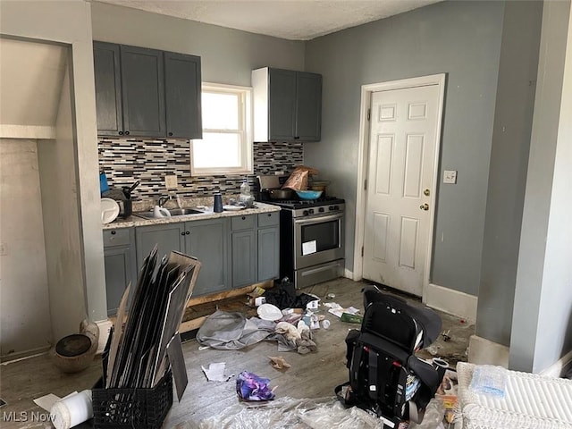 kitchen with baseboards, a sink, decorative backsplash, gray cabinetry, and stainless steel gas range oven