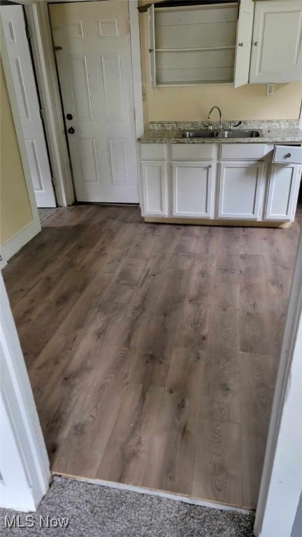 kitchen with light stone counters, white cabinets, wood finished floors, and a sink