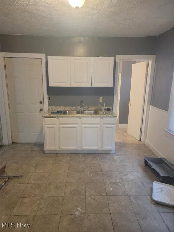 kitchen with white cabinets, a textured ceiling, and a sink