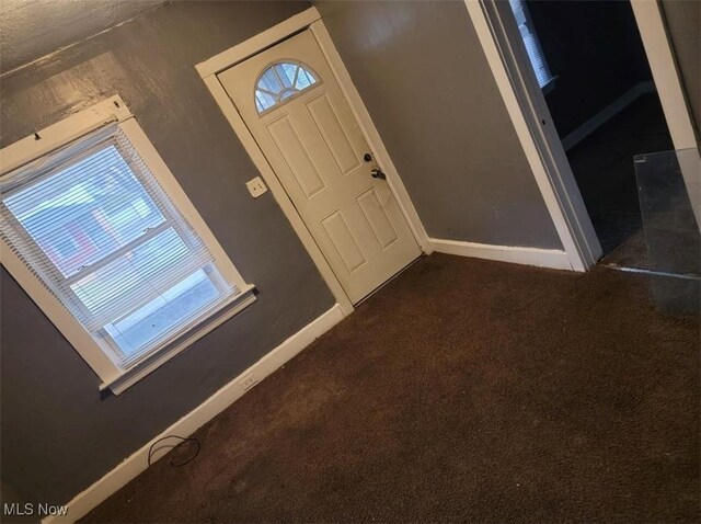 foyer entrance with baseboards and dark colored carpet