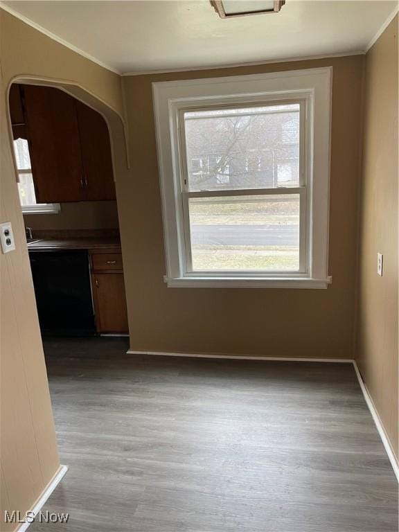 unfurnished dining area with arched walkways, light wood-style floors, baseboards, and ornamental molding