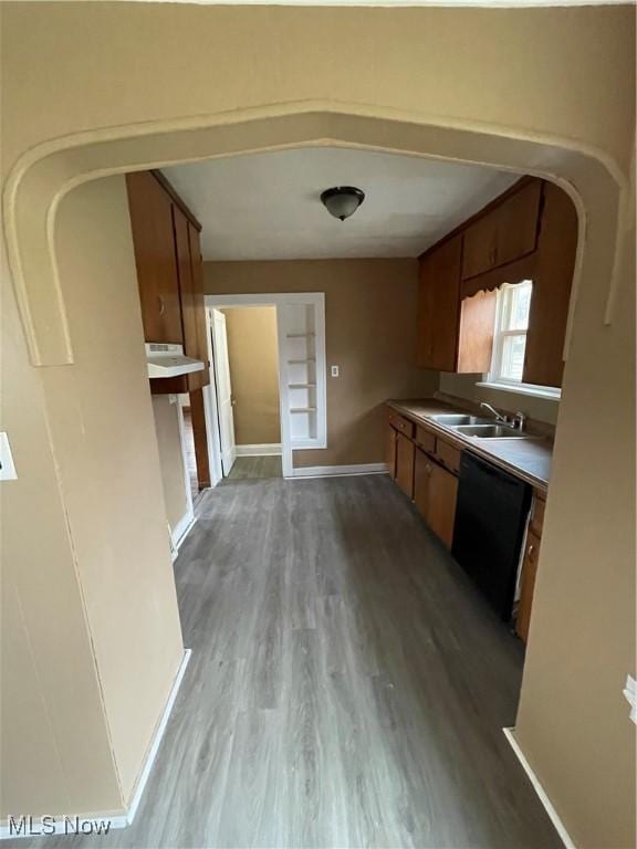 kitchen featuring a sink, black dishwasher, wood finished floors, arched walkways, and brown cabinetry