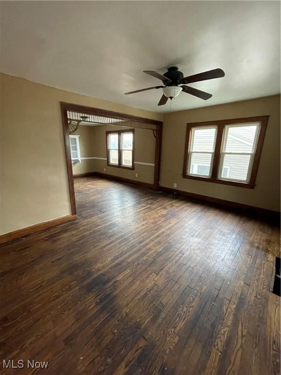 unfurnished room with dark wood finished floors, a ceiling fan, and baseboards