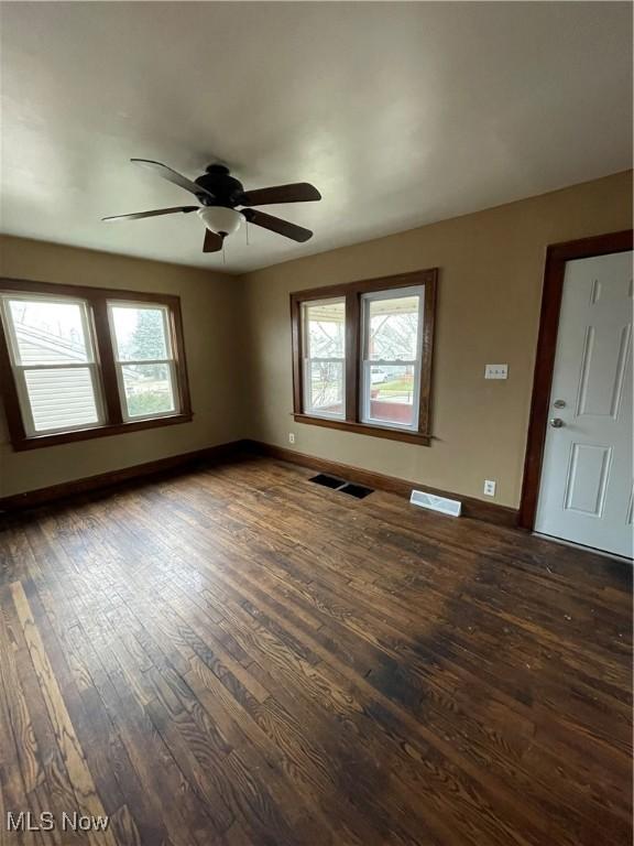 unfurnished room featuring a ceiling fan, visible vents, dark wood-style floors, and baseboards