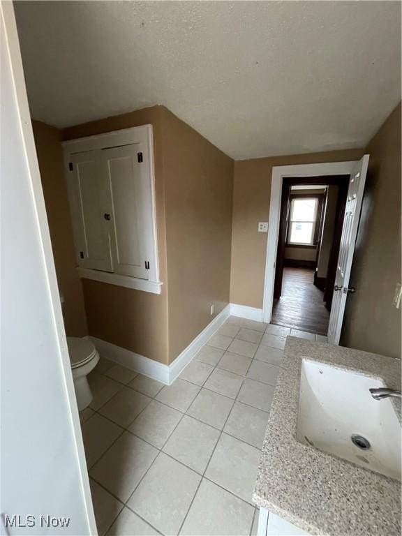 bathroom featuring baseboards, a sink, tile patterned flooring, a textured ceiling, and toilet