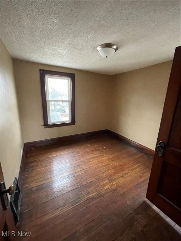 unfurnished room with a textured ceiling, dark wood-type flooring, and baseboards