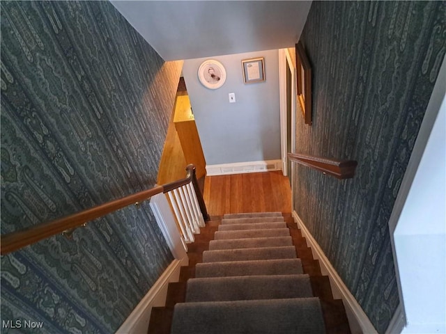 stairs featuring baseboards, wood finished floors, an accent wall, and wallpapered walls