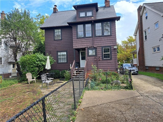 american foursquare style home with roof with shingles, a fenced front yard, and a chimney