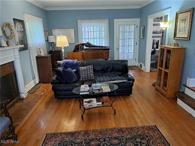 living room featuring a brick fireplace, wood finished floors, and ornamental molding