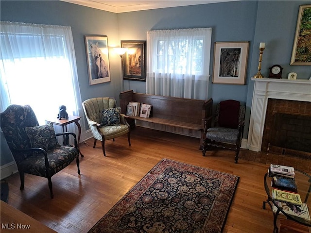 sitting room with crown molding, a fireplace with flush hearth, wood finished floors, and baseboards