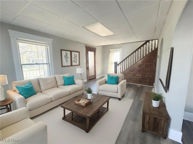 living room with stairway, a paneled ceiling, baseboards, and wood finished floors