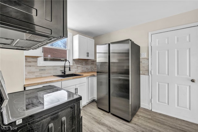 kitchen featuring butcher block countertops, electric range oven, freestanding refrigerator, white cabinets, and a sink