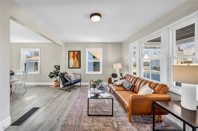 living area featuring visible vents, baseboards, a healthy amount of sunlight, and wood finished floors